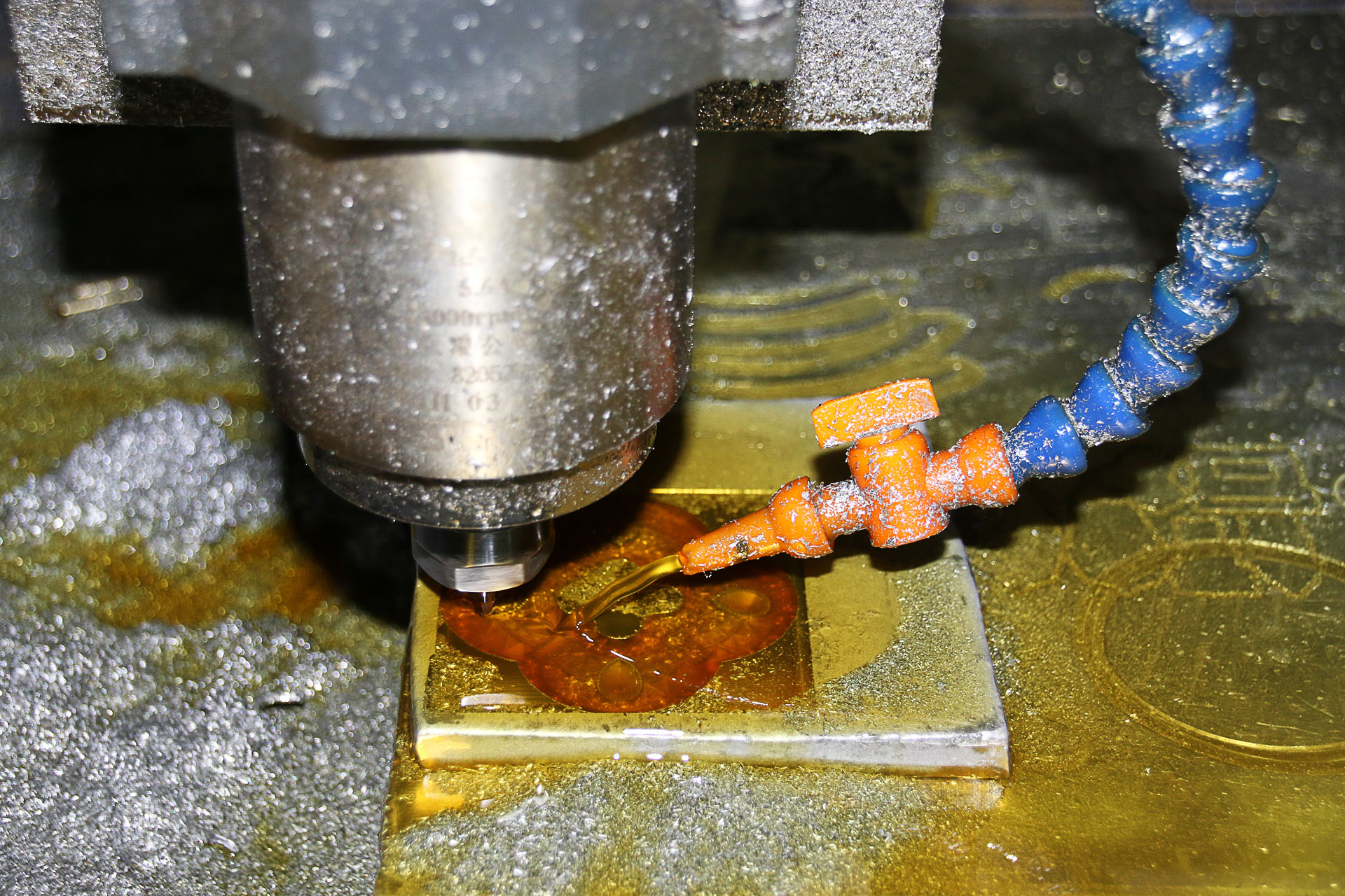 A CNC milling spindle cutting a brass plate under coolant